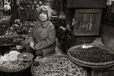 Black and white photograph of a woman selling vegetables in the wet market in Pyin Oo Lwin, Myanmar. 