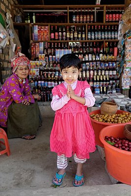 Color photograph of a young girl greeting visitors to her grandmother's wine shop in Pyin Oo Lwin, Myanmar. 