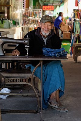 Photograph of a tailor wearing a blue longyi in the market at Pyin Oo Lwin, Myanmar. 