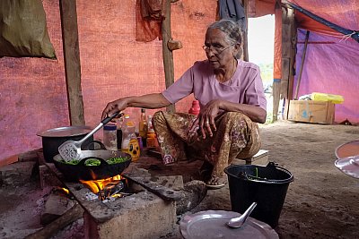 Photograph of a woman preparing vegetables over an open fire in Myanmar. 
