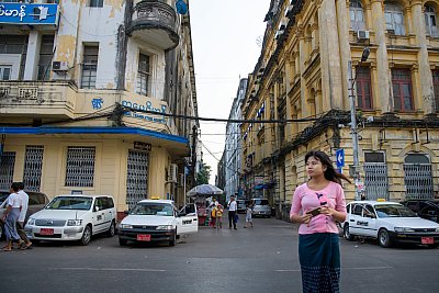Photo of a young woman in a pink blouse crossing the street in Yangon, Myanmar. 