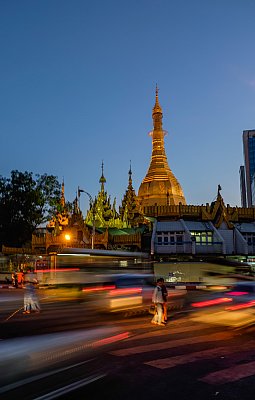 Color photograph of a pogoda and street scene with rushing cars in Yangon, Myanmar. 
